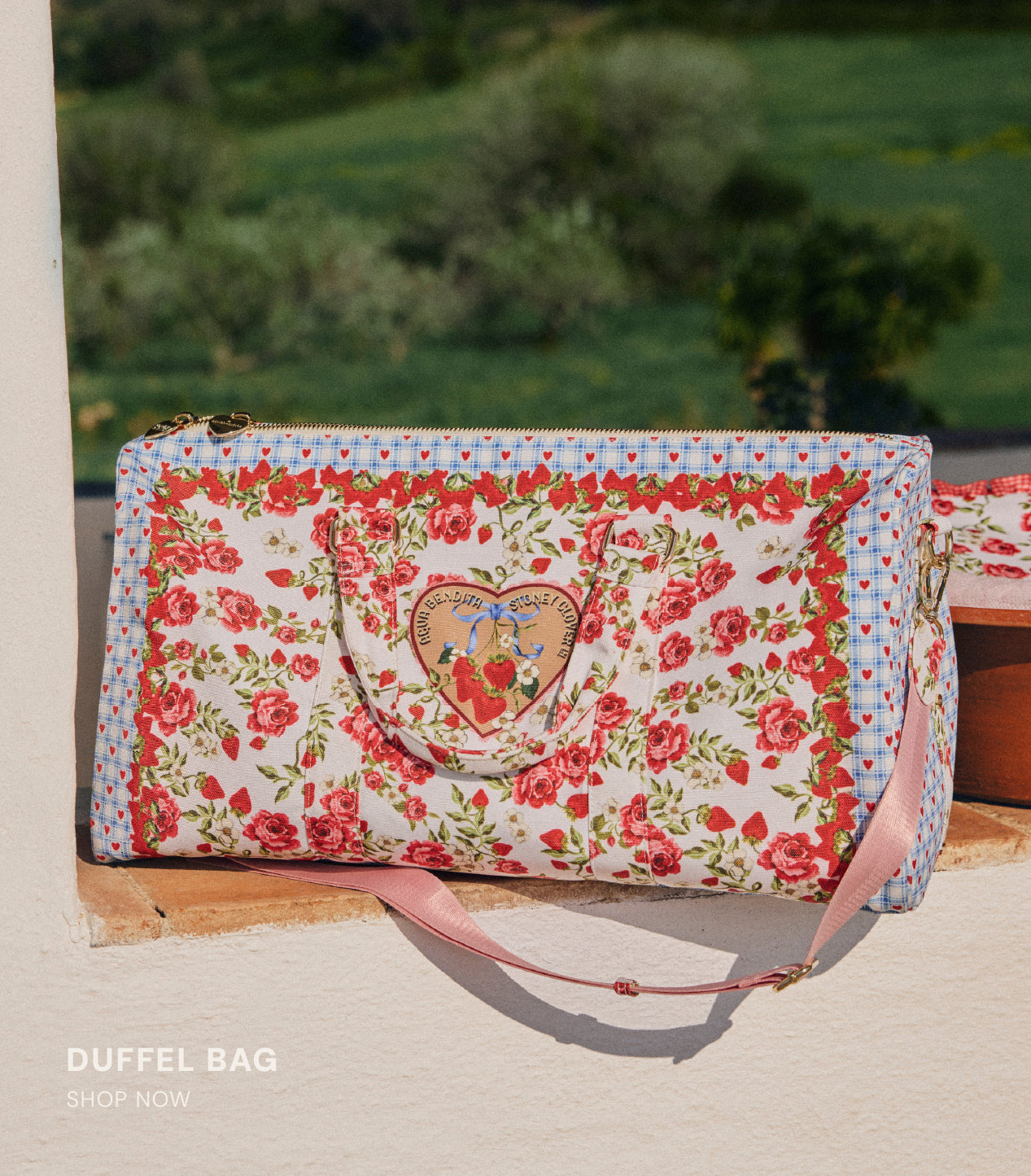 Floral duffel bag with a heart design on a sandy surface with greenery in the background