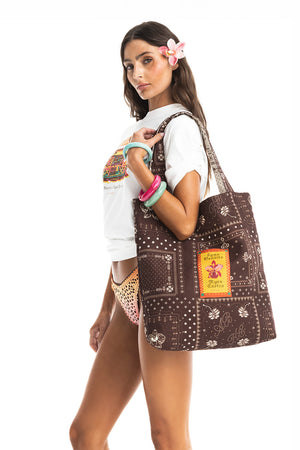 Woman wearing a white T-shirt and carrying a brown printed tote bag.