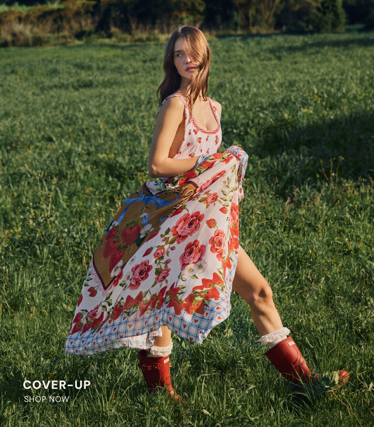 Woman in a floral dress and red boots standing in a field with a cover-up draped over her.