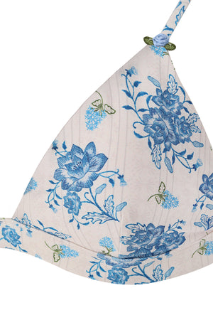 Close-up detail of a blue floral triangle bikini top featuring an ivory base, intricate blue botanical print, and delicate blue rose appliqué accents on the straps.